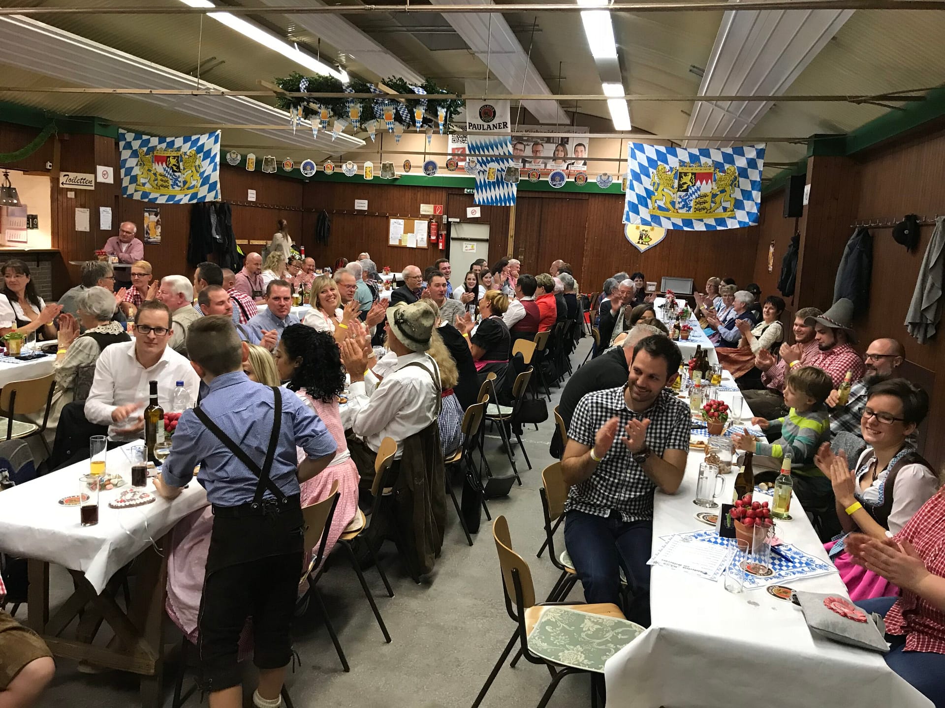 Menschen in traditioneller bayerischer Tracht bei einer Veranstaltung in einem festlich dekorierten Saal.