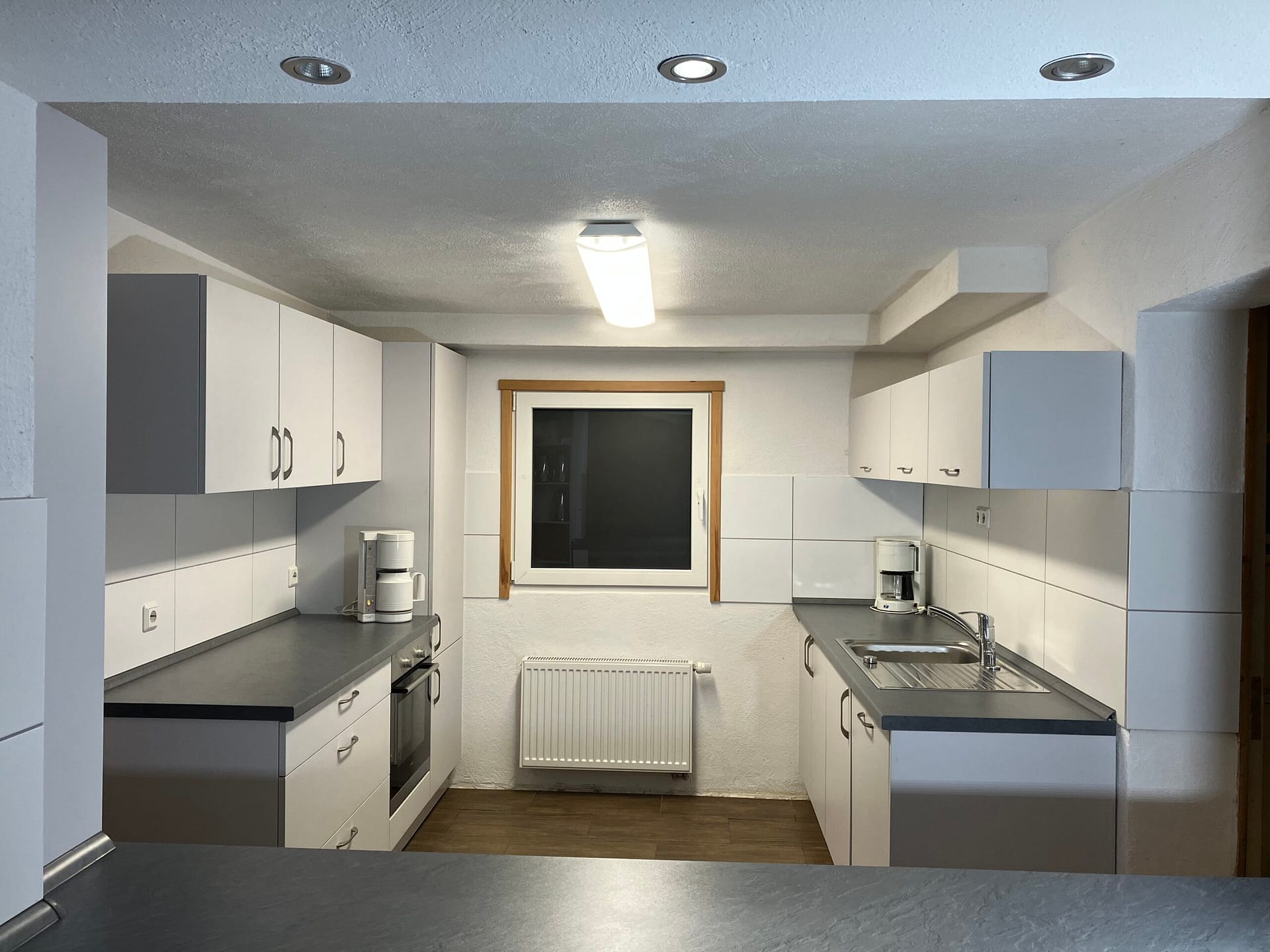 Moderne Küche mit weißen Schränken, Edelstahlspüle und Fenster zur natürlichen Beleuchtung.