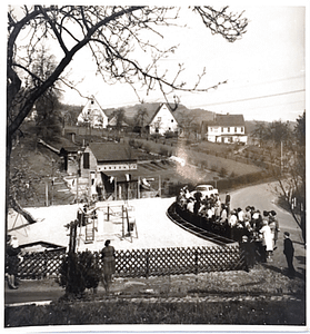 Schwarz-weiß Foto einer Menschenmenge, die sich um einen Spielplatz versammelt.