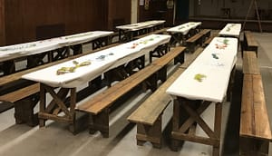 Reihen von Holztischen mit weißen Tischdecken und bunten Dekorationen in einem Innenraum.