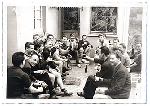 Eine Gruppe von Männern sitzt zusammen und hält Getränke in der Hand, während sie in die Kamera schauen.