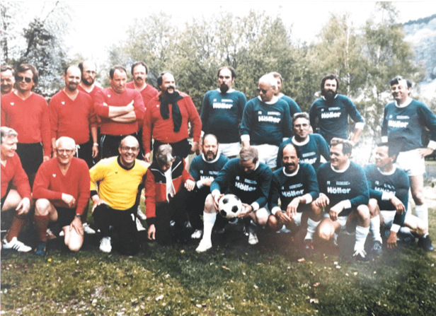 Gruppenfoto einer Fußballmannschaft mit Spielern in roten und grünen Trikots auf einem Rasen.