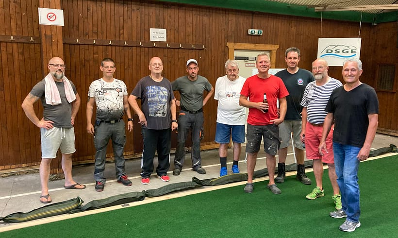 Gruppe von acht Personen, die in einer Indoor-Boule-Bahn stehen und in die Kamera lächeln.